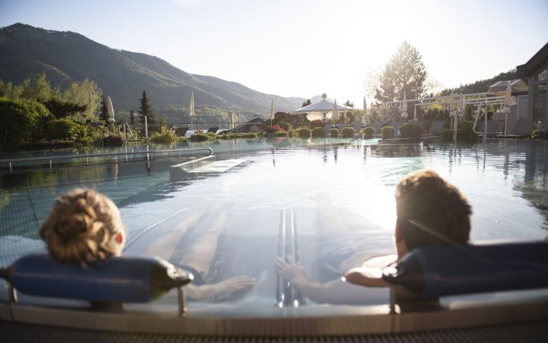 Zwei Gäste liegen im Aussenpool mit Blick auf die Umgebung im Waldhof Fuschlsee Resort