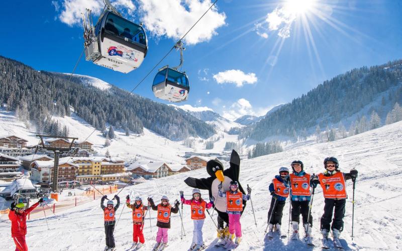 Eine Kinder-Schigruppe auf der Piste mit Blick auf die Gondeln beim Familienhotel Zauchenseehof