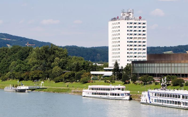 Aussenansicht des ARCOTEL Nike Linz Hotels mit der Donau im Vordergrund