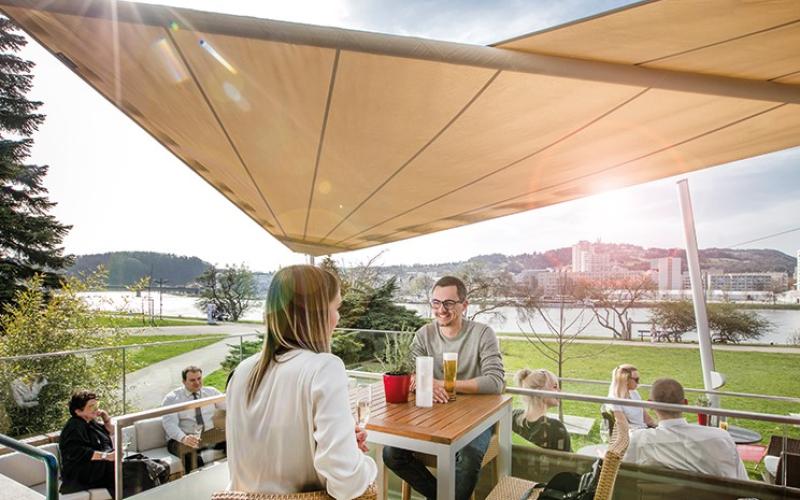 Mehrere Gäste sitzen auf der Sonnenterrasse mit Sonnensegel im ARCOTEL Nike Linz