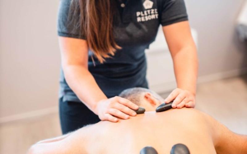 Ein Gast genießt eine Hot-Stone Behandlung durch eine Therapeutim im DAS WALCHSEE Sportresort