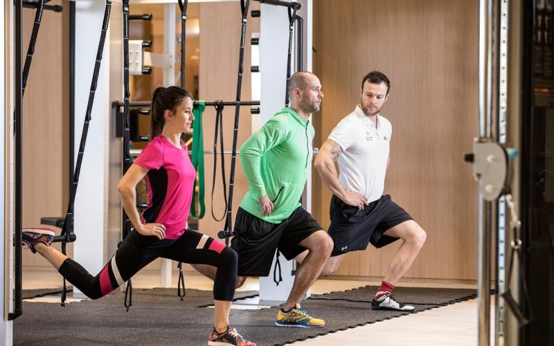Zwei Gäste trainieren mit einem Personal Trainer im Fitnessbereich des Das Hohe Salve Sportresorts