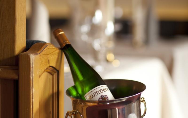 Eine Flasche Wein im Weinkühler im Restaurant mit gedeckten Tischen im Kulinarik und Genießerhotel Alpin