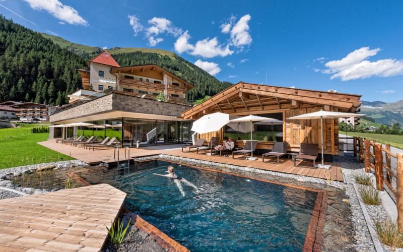 Ansicht des Aussenpools mir Badehaus und dem Alpinhotel berghaus im Hintergrund