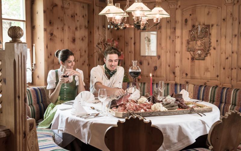Blick in das Restaurant mit einer Brettljause am Tisch und 2 Gästen im Hotel Alpina