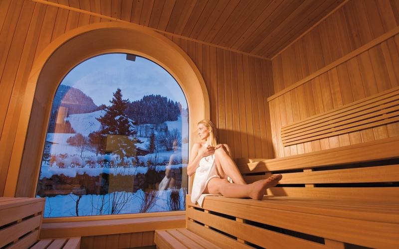 Eine Dame in der Sauna mit Blick in die Winterlandschaft rund um den Rasmushof Kitzbühel