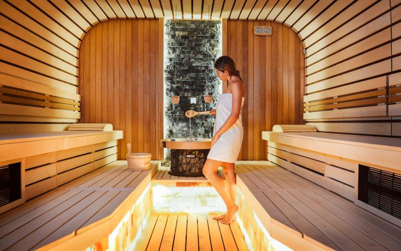 Eine Frau in Handtuch gießt Wasser über die Heizsteine in der Sauna des Grifid Hotel Encanto Beach MEDI SPA