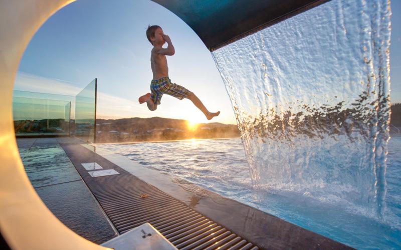 Ein Junge springt in den Aussenpool des AIGO Familien und Sport Resorts