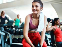 Junge Frau in einem Fitness Center, im Hintergrund trainieren 3 Frauen an Gewichten
