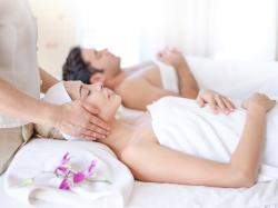 Paar neben einander auf Massagetische liegend, die Frau erhält eine Kopfmassage