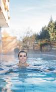 Eine Dame schwimmt im Aussenpool des Hotels GUT Trattlerhof und Chalets